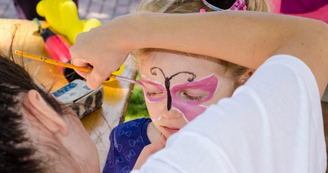 Bambina con viso dipinto come farfalla rosa e nero, artista che la trucca.