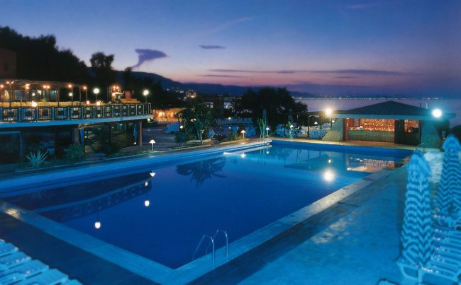 Piscina illuminata al tramonto con vista sul mare e luci soffuse.