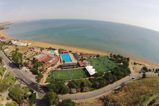 Vista aerea di un resort con piscine e campi sportivi vicino al mare.