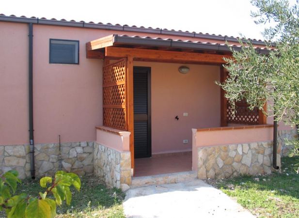 Ingresso di una casa rosa con tettoia in legno e muretto di pietra.
