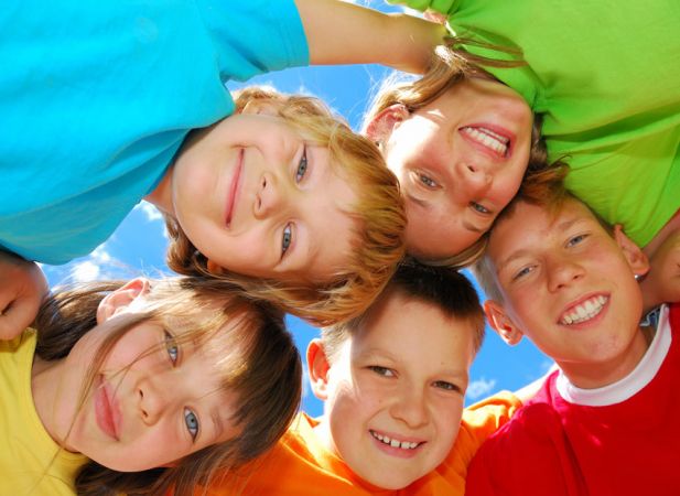 Gruppo di bambini sorridenti ripresi dal basso contro il cielo blu.
