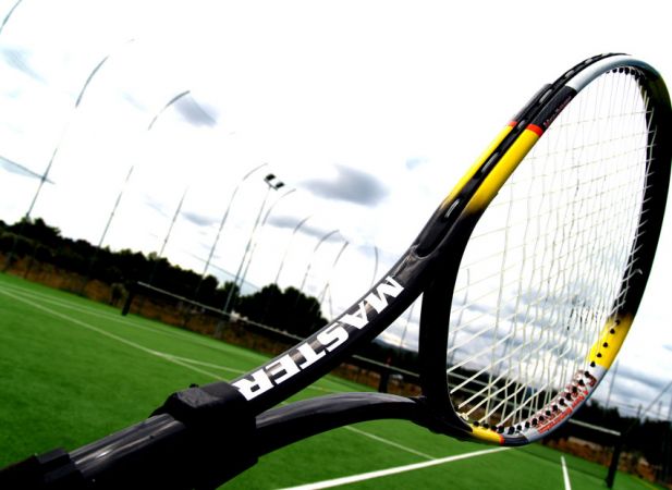Racchetta da tennis su un campo verde all'aperto sotto un cielo nuvoloso.