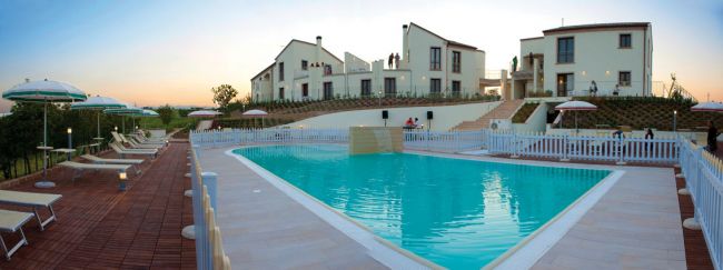 Piscina con sdraio e ombrelloni, davanti a edifici moderni all'alba o al tramonto.