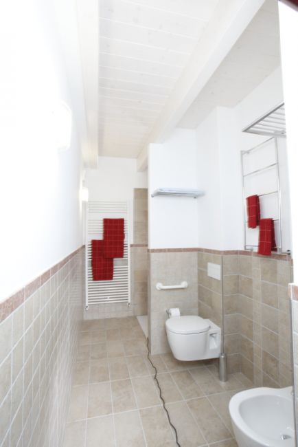 Un bagno moderno con piastrelle beige, asciugamani rossi e servizi igienici.