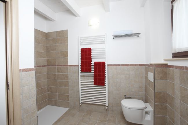 Un bagno con piastrelle beige, doccia aperta, scaldasalviette bianco e asciugamani rossi.