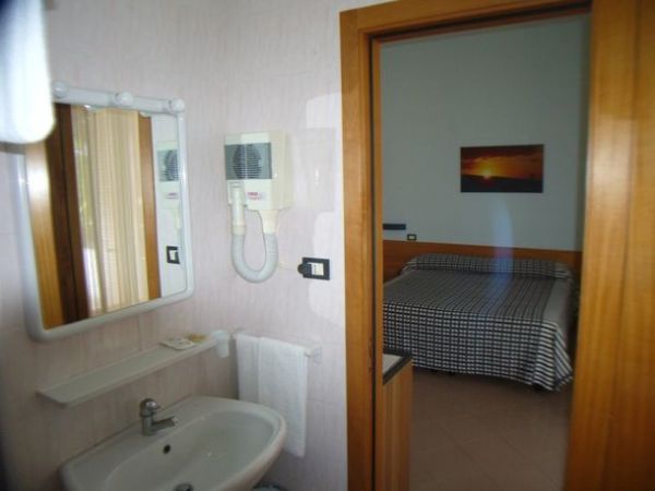 Bagno con specchio, asciugacapelli e vista su camera da letto con letto matrimoniale.