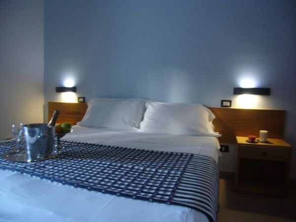 Letto matrimoniale con testiera in legno e luci soffuse.