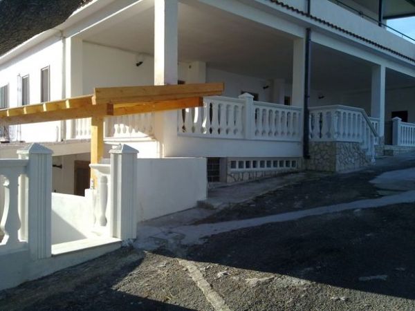 Una villa bianca con balconi e muretto sul davanti, situata su una strada in pendenza.