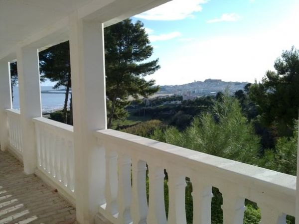 Vista dalla terrazza su una vallata con alberi, un villaggio lontano e il mare in lontananza.