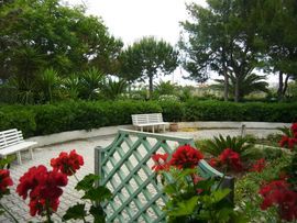 Un giardino con panchine bianche e fiori rossi in primo piano.