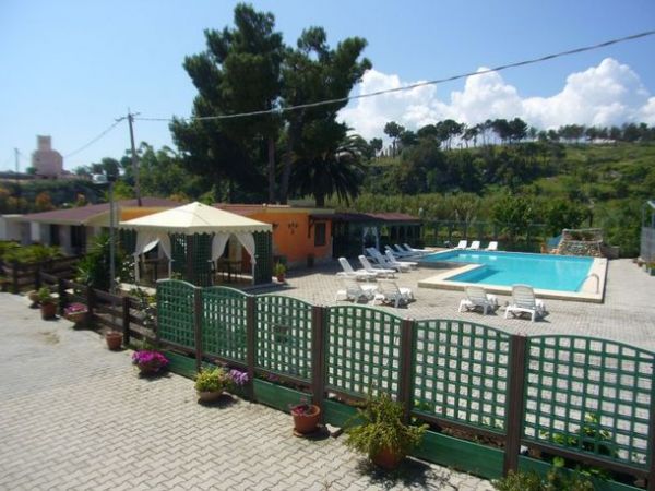 Area piscina all'aperto con lettini, ombrellone e siepi verdi.