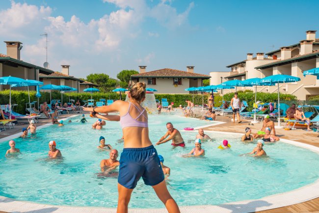 Persone fanno acquagym in piscina sotto un cielo sereno.