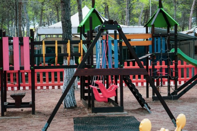 Area giochi con altalene colorate e staccionata.