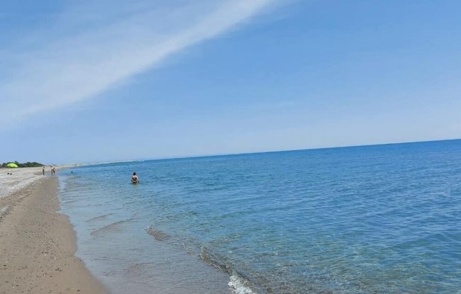 Spiaggia sabbiosa con mare calmo e cielo sereno.
