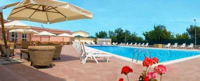 Piscina all'aperto con lettini e ombrelloni, circondata da sedie in vimini e piante.