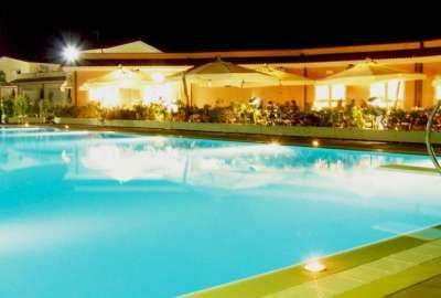 Piscina illuminata di notte con tavoli e ombrelloni, atmosfera calda e accogliente.