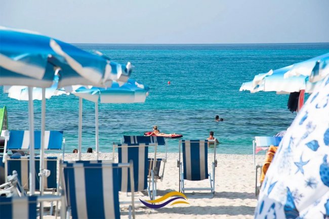 Sdraio e ombrelloni sulla spiaggia con mare azzurro.