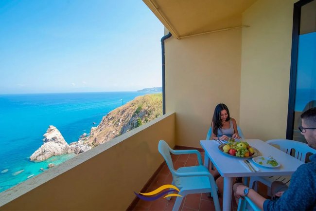 Balcone con vista mare, tavolo e due persone.