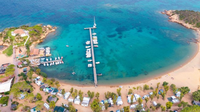 Veduta aerea di un molo con barche e campeggio sulla spiaggia.