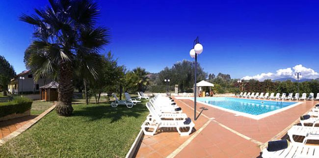 Piscina all'aperto di giorno con lettini e palme.