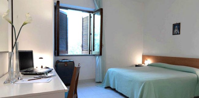 Stanza con letto singolo, scrivania con computer, valigia e finestra aperta.