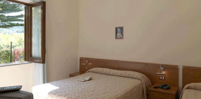 Camera con due letti singoli, libro sul letto e finestra con vista alberi.