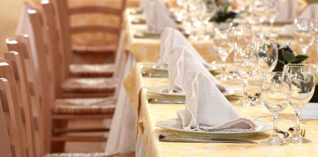 Dettaglio di un tavolo con tovaglia gialla, tovaglioli piegati e bicchieri di vetro.