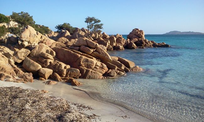 Spiaggia con grandi rocce marroni, sabbia chiara e mare cristallino.