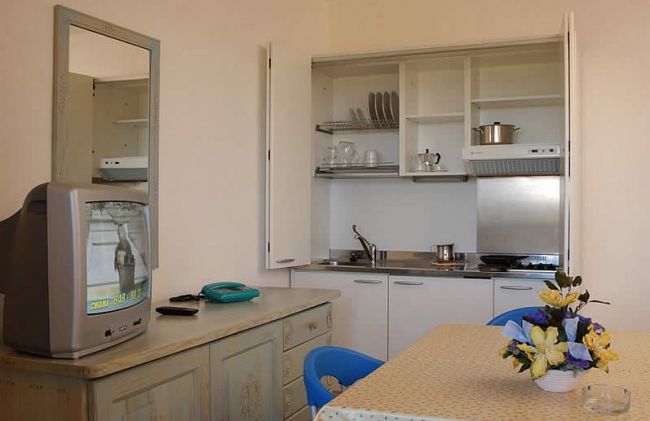 Un angolo cottura con ripiani aperti, un tavolo con fiori e una TV su un mobile accanto.