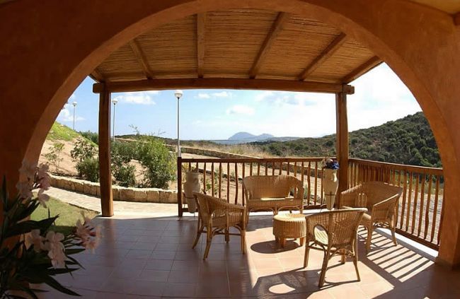 Una veranda coperta con mobili di vimini e vista su colline verdi.