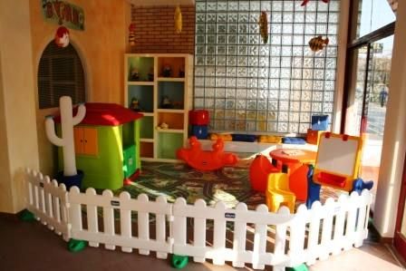 Un'area giochi per bambini con casetta, recinzione e giochi colorati.