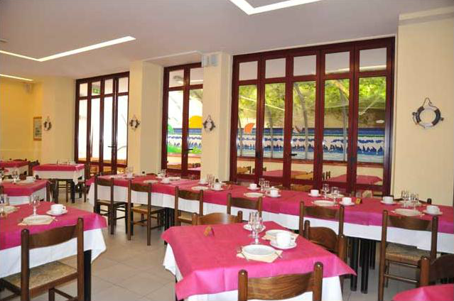 Sala da pranzo con tavoli apparecchiati, tovaglie rosa e finestre ampie.
