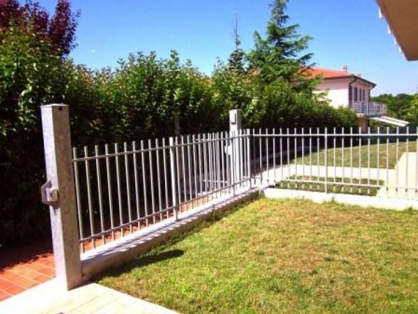 Giardino con erba e recinzione metallica, circondato da cespugli verdi.
