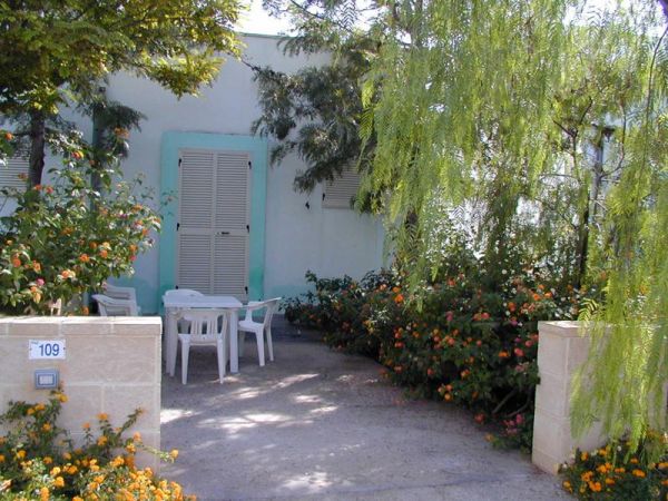 Patio con tavolo e sedie, circondato da piante e fiori.