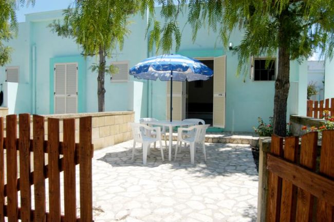 Cortile con tavolo, sedie bianche e ombrellone blu.