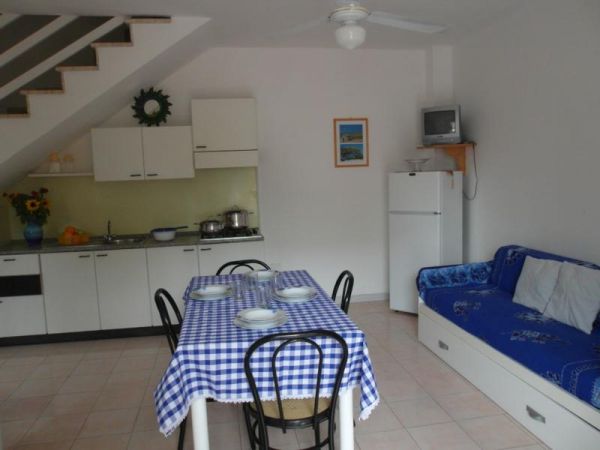 Cucina bianca con tavolo, sedie e divano blu.