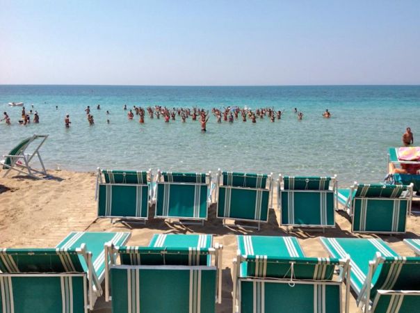 Sedie a sdraio vuote davanti al mare con bagnanti in acqua.