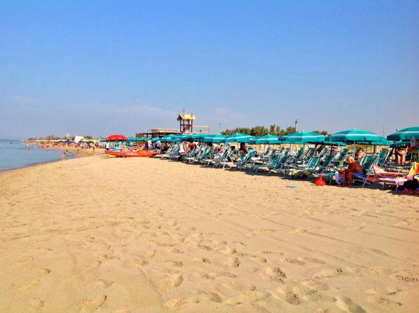 Spiaggia sabbiosa con sdraio e ombrelloni turchesi.