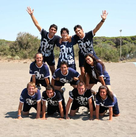 Un gruppo di persone forma una piramide umana sulla spiaggia, tutti indossano magliette blu.