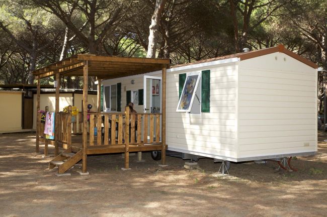 Una roulotte bianca con veranda in legno tra gli alberi.