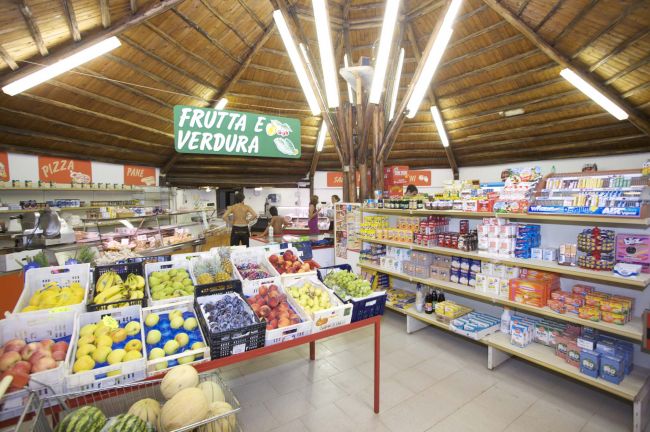Interno di un negozio con frutta, verdura e scaffali di vari prodotti alimentari.