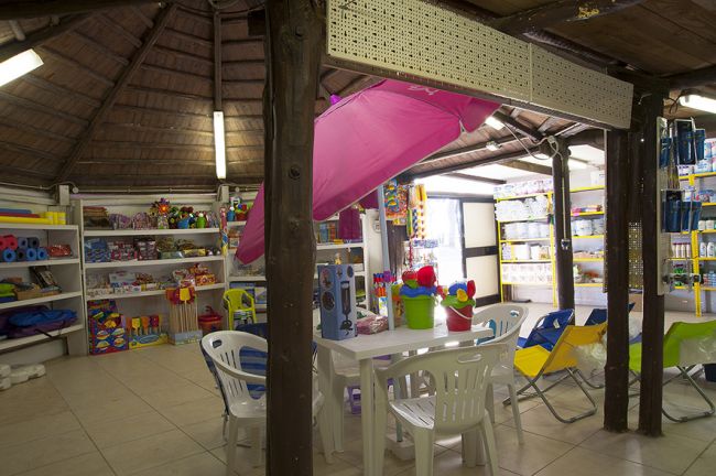 Un negozio con scaffali di giochi e articoli vari, tavolo con sedie al centro.