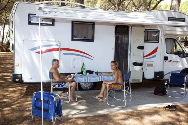 Camper con due persone sedute a un tavolo esterno.