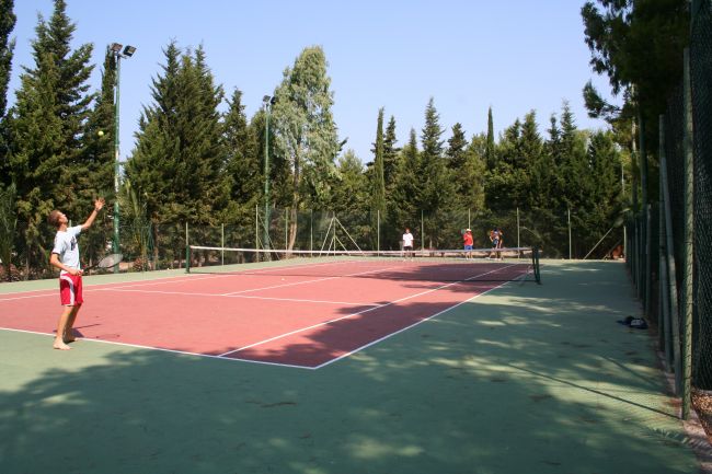 Campo da tennis all'aperto con giocatori. Alberi sullo sfondo.