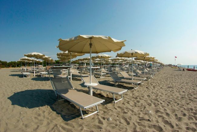 Spiaggia sabbiosa con lettini e ombrelloni.