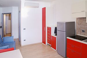 Angolo cottura con mobili rossi, frigo grigio e divano blu.