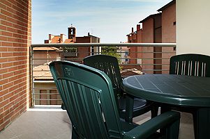 Balcone con tavolo e sedie verdi, vista su tetti di edifici e cielo azzurro.