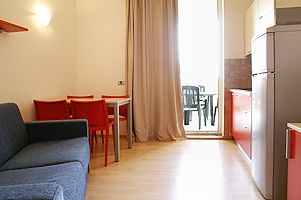 Soggiorno con divano blu, tavolo e sedie rosse, luce soffusa, tende beige.