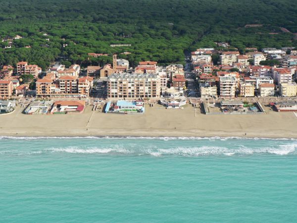 Vista aerea di una spiaggia con edifici residenziali e una foresta sullo sfondo.