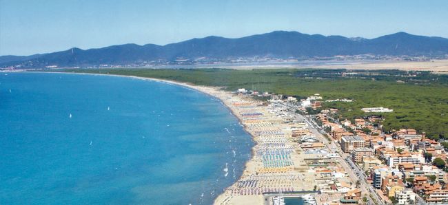 Panorama di una lunga spiaggia affollata da ombrelloni, con montagne sullo sfondo.